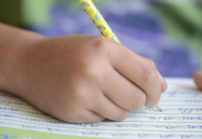 Mão de criança escrevendo para representar as cooperativas educacionais